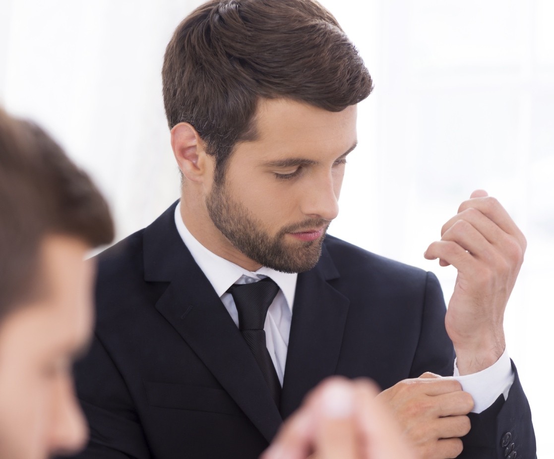 Everything should be perfect. Handsome young man in formalwear adjusting his sleeves while standing against mirror.jpg